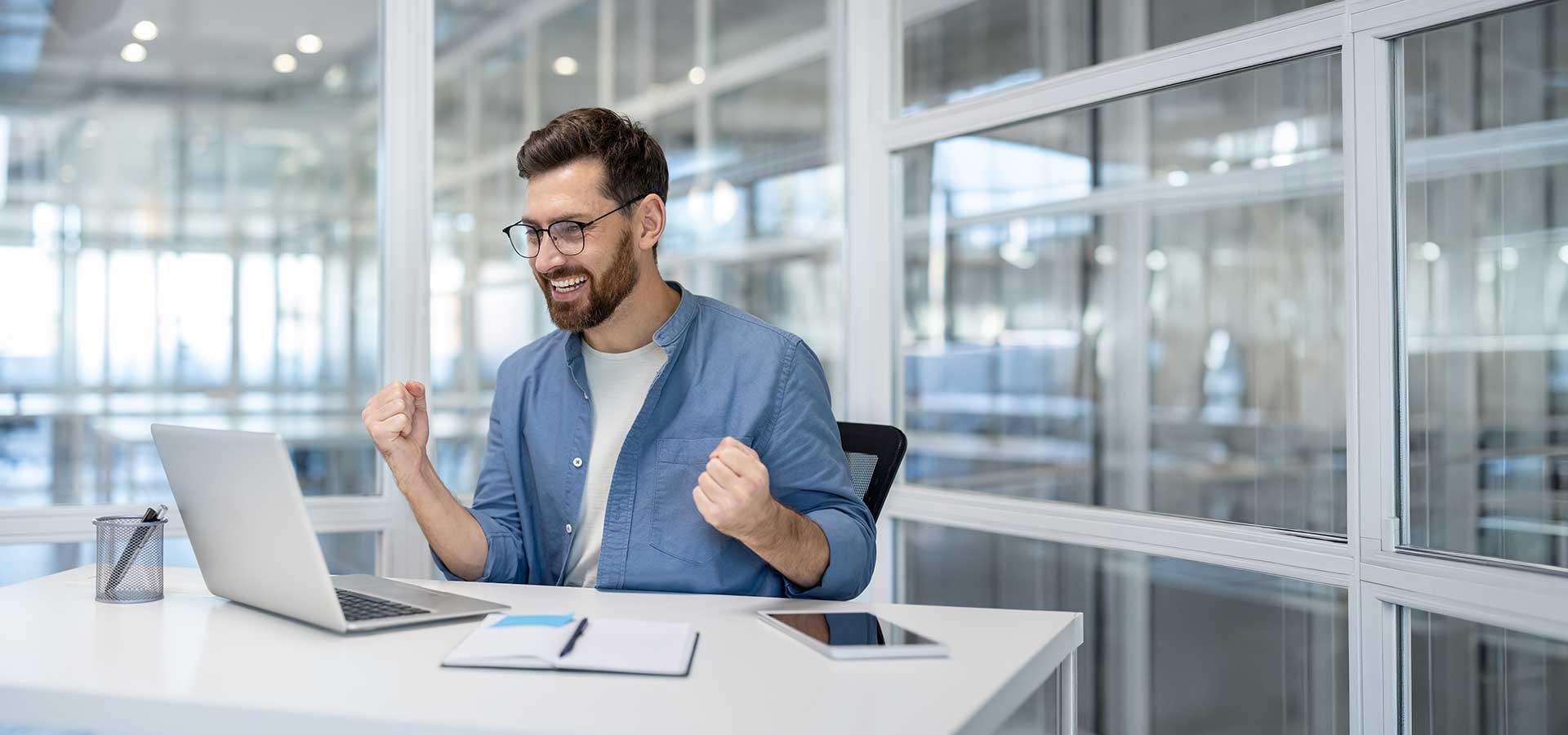 Mann freut sich am Schreibtisch mit funktionierendem Computer